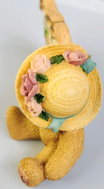 Yellow teddy bear with a decorative straw hat featuring flowers on a light gray background