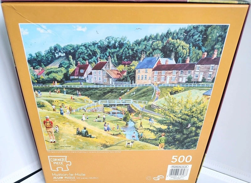 A 500-piece jigsaw puzzle box by Corner Piece, featuring a colorful illustration of Hutton-le-Hole village and park with people, trees, and cottages. The box has a warm tan border and is photographed standing upright against a white background.