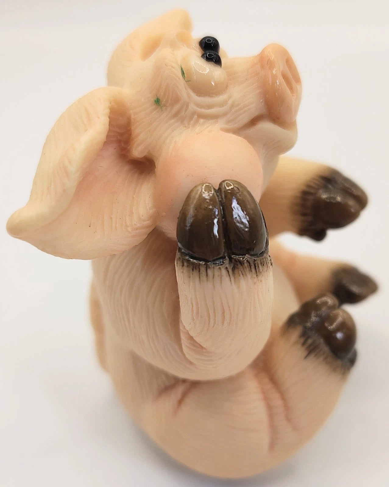 A small sculpted figurine of a pig lying on its back, with dark brown hooves and a glossy finish, photographed against a plain white background.