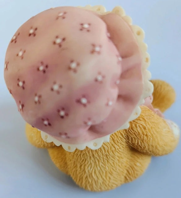 Cherished Teddies Cherish resembling a bear with a pink flower on its head against a light blue.background