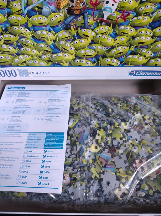 A Clementon 1000-piece jigsaw puzzle featuring a dense pattern of green Toy Story aliens, shown with its instruction sheet and a bag of loose puzzle pieces in a clear plastic bag.