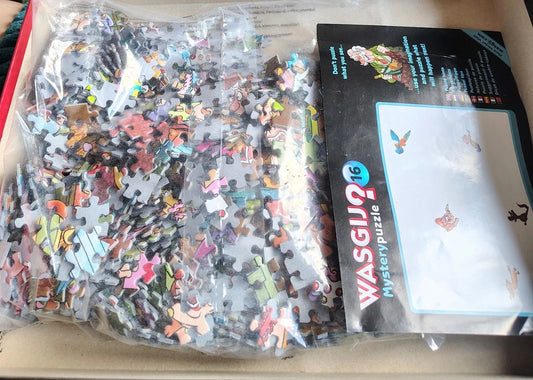 A clear plastic bag filled with many small multicolored jigsaw puzzle pieces placed next to a black product box labeled WASGIJ 16 Mysterypuzzle.