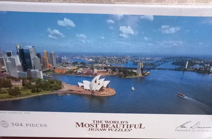 Jigsaw puzzle box with a scenic view of a city, including a bridge and opera house.
