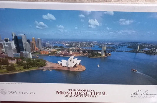 Jigsaw puzzle box with a scenic view of a city, including a bridge and opera house.
