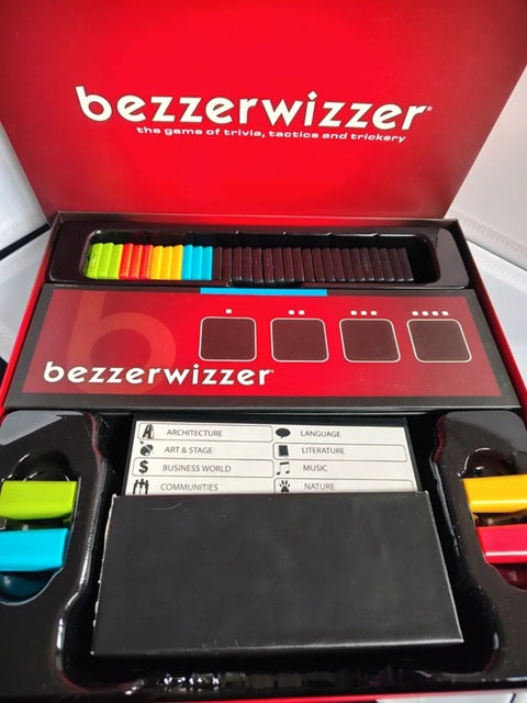 The 'bezzерwizzer' game board and components shown inside its red packaging box. The open box reveals the red game board, a black playmat, colorful cards, and game pieces.