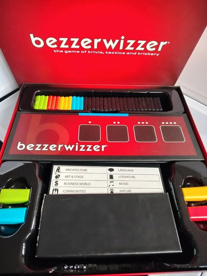 The 'bezzерwizzer' game board and components shown inside its red packaging box. The open box reveals the red game board, a black playmat, colorful cards, and game pieces.