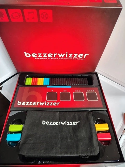 Bezzerwizzer game set shown open in its red retail box, with the game board, colored pieces, and a black branded carrying pouch visible.