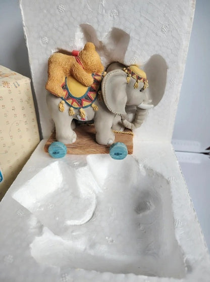 A small decorative elephant figurine with a yellow saddle and colorful patterned details, displayed inside a white foam insert of its packaging box.