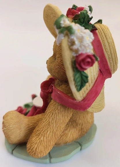 Decorative bear figurine with floral headpiece and red ribbon on a white background