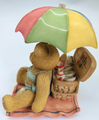 Teddy bear with a colorful umbrella, swimsuit, and picnic basket on a white background