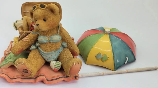 Teddy bear in swimsuit with a beach umbrella and towel on a white background