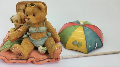 Teddy bear in swimsuit with a beach umbrella and towel on a white background