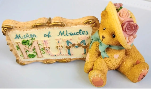 Yellow teddy bear with a decorative hat and 'Mother of Miracles Mum' sign on a white background