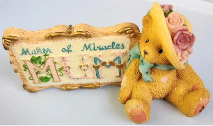 Yellow teddy bear with a decorative hat and 'Mother of Miracles Mum' sign on a white background