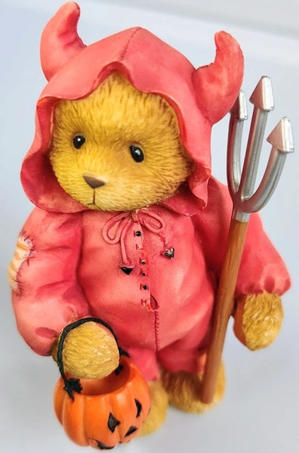 Teddy bear dressed as a devil with a pink hood, trident, and pumpkin on a white background