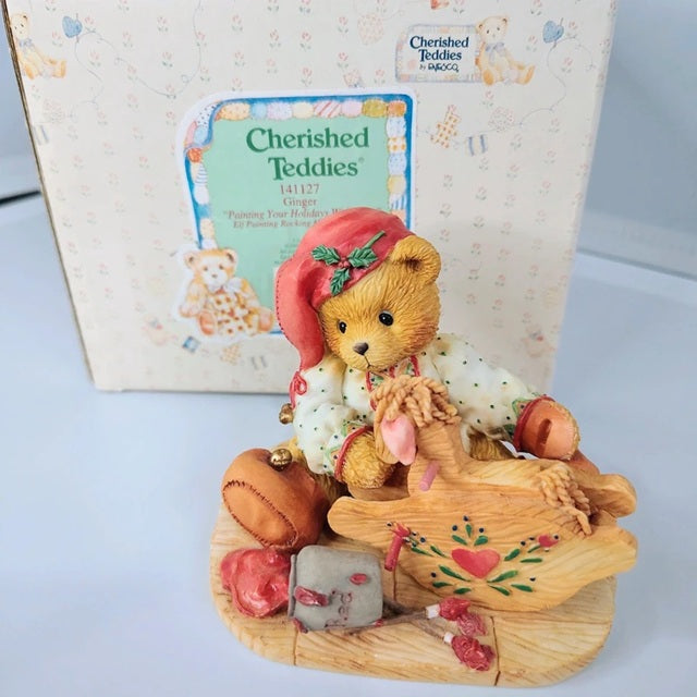 Cherished Teddies figurine with a teddy bear on a wooden platform, in front of a Cherished Teddies box.