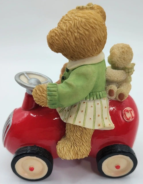 Teddy bear driving a red toy car with another teddy bear in the back on a white background