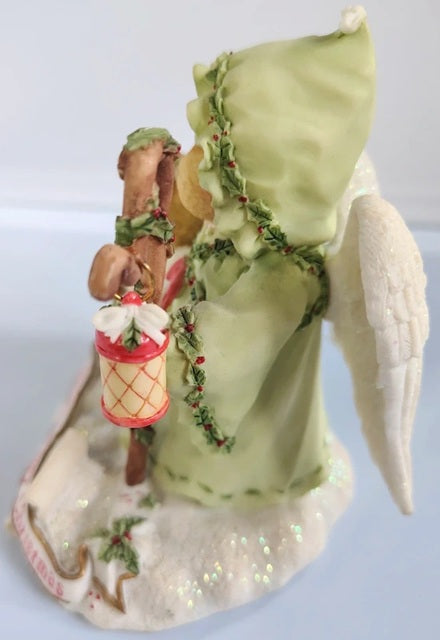 Decorative angel figurine with a green dress and lantern on a light blue background