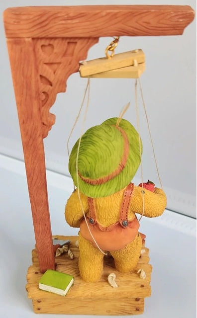 Decorative figure of a teddy bear with a green head on a wooden swing against a white background