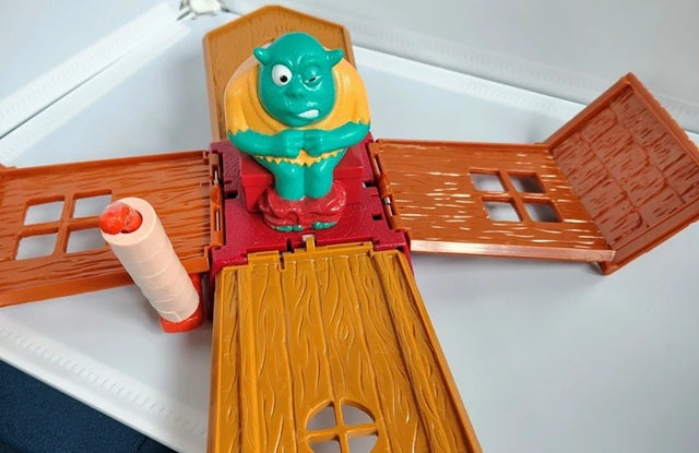 Toy figure of a green creature in a red and brown playset on a white surface
