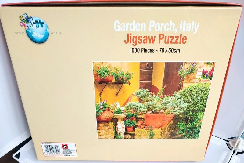 Boxed jigsaw puzzle titled "Garden Porch, Italy" with 1000 pieces, shown against a light background. The beige box features a photo of a colorful Italian garden porch scene and the brand logo "Puzzle World" on the upper left.
