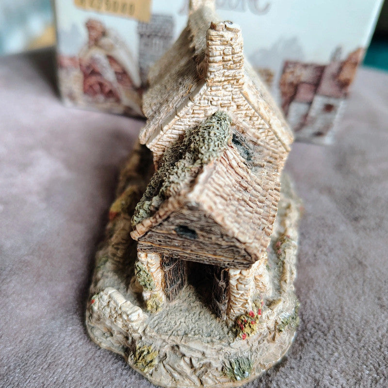 Small model of a rustic house with a thatched roof on a textured surface.