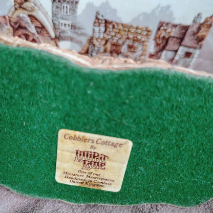 Green fabric with a label from Cobbler's Cottage by Lilliput Lane, featuring miniature landscapes.
