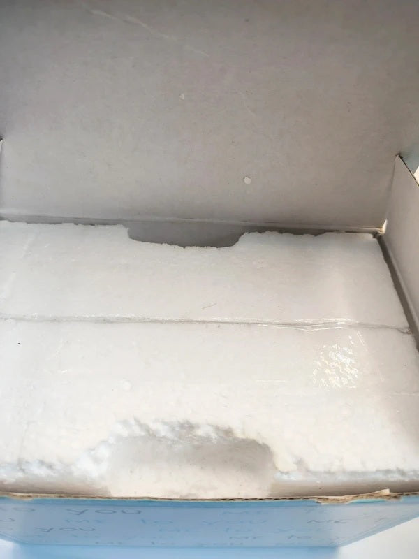 A close-up view inside a cardboard box showing white foam padding and a light blue outer box edge.