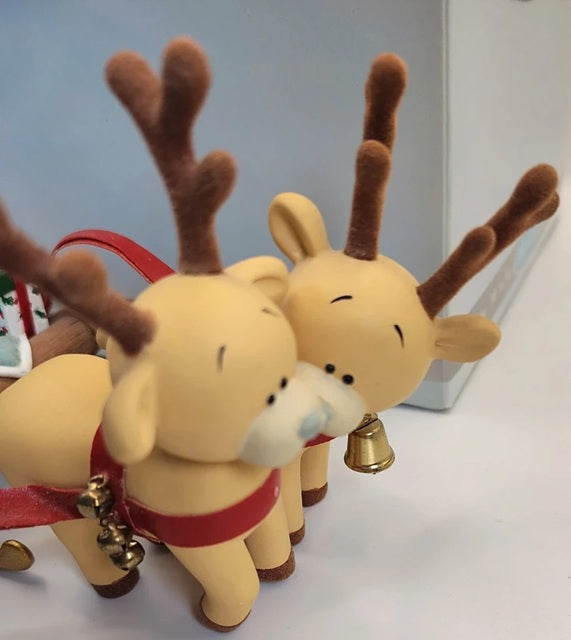 Two small resin reindeer ornaments with brown antlers, cream bodies, red harnesses, and small gold bells, photographed close up on a light surface.