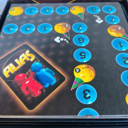 Board game box for 'Alias' with colorful characters and numbers on a dark background