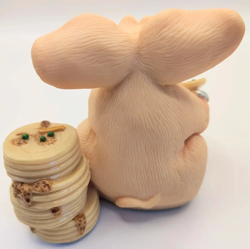 A beige pig figurine sitting next to a small stack of round, similarly colored discs with small green and brown details, photographed on a plain white background.