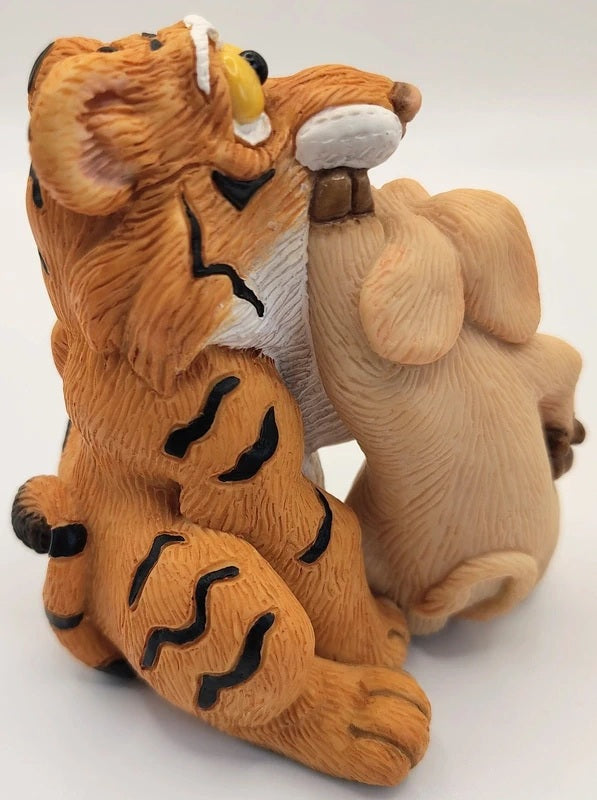A small figurine of a tiger sitting and biting a rabbit, shown on a plain white background.