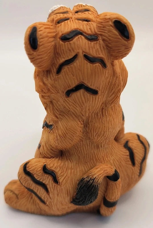 A small sitting tiger figurine with a textured orange-brown body and black stripes, photographed against a plain light background.