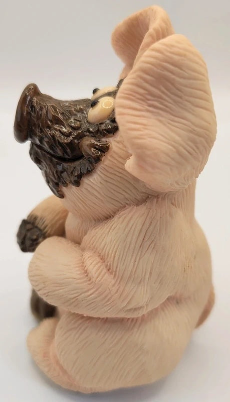 A small sculpted pig figurine with a textured, ribbed surface resembling fur or hide, featuring a dark brown snout, hooves, and a small cream-colored eye detail, set against a plain white background.