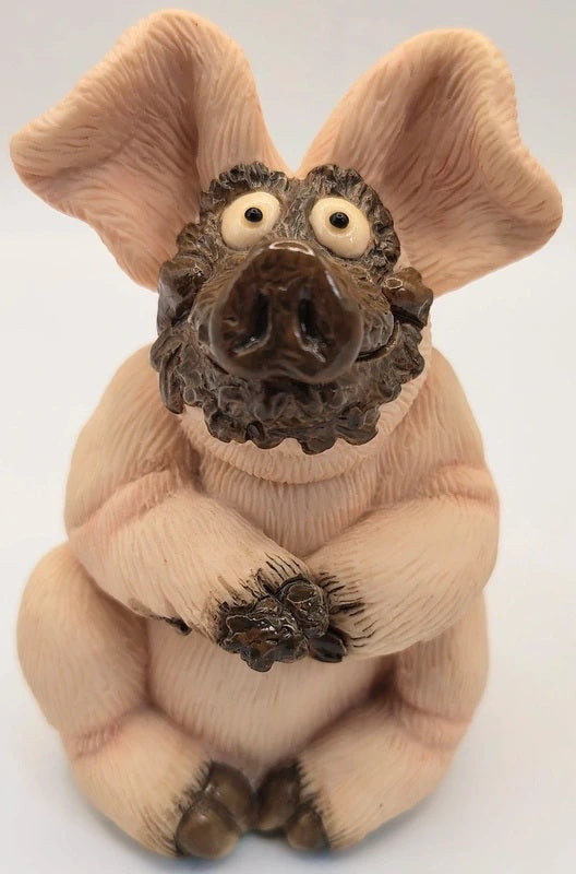 Piggin Gorgeous figurine handmade by David Corbridge in 1997. A whimsical pig figurine sitting upright, featuring a textured light pink body, large floppy ears, a dark brown snout, and a scruffy dark brown beard, with small white eyes and dark claws, set against a plain white background.