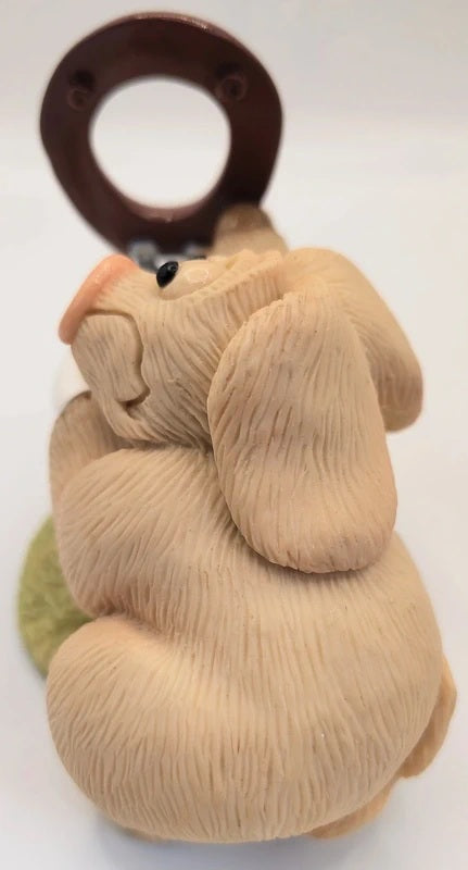 A beige textured ceramic pig figurine holding a dark brown wooden toilet set, set against a plain white background.