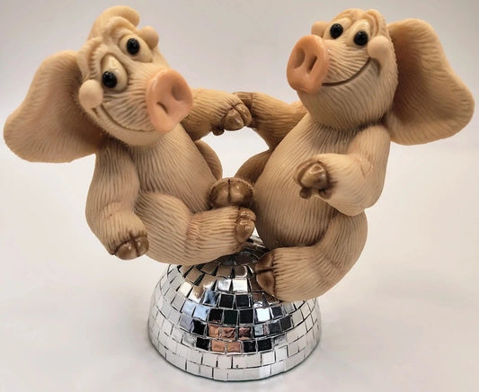 A decorative figurine of two dancing pigs sitting on a mirrored disco ball base, photographed against a plain light background. Piggin Night Fever figurine.