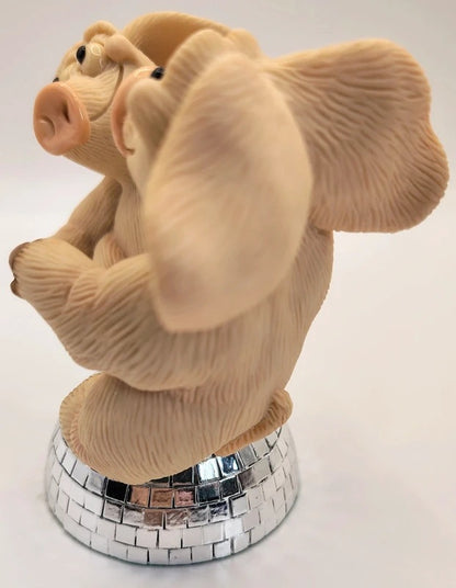 A beige sculpted pig figurine with textured fur, posed sitting on a mirrored silver disco-ball base against a plain white background.