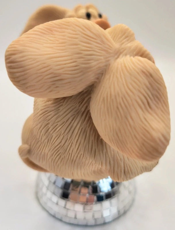 A beige textured pig figurine with large  ears, shown from the back on a mirrored silver base against a plain light background.
