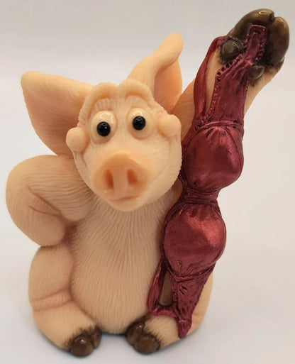 Piggin Sexy figurine handmade by David Corbridge in 1999. A pig figurine with a shiny dark red satin dress, posed against a plain light background.