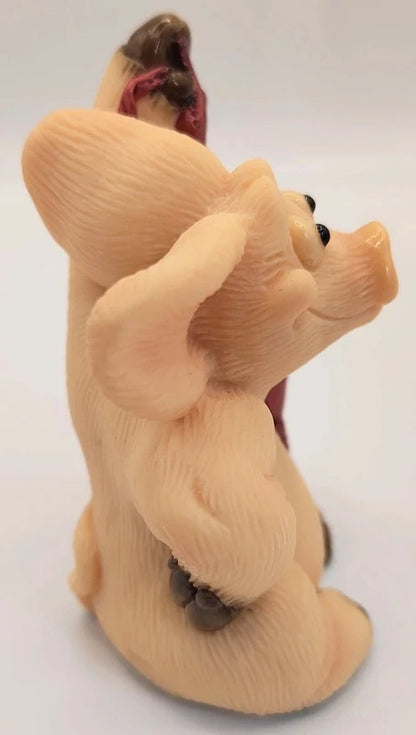 A small figurine of a light peach-colored pig looking back over its shoulder, with a dark brown snout and small dark accents, set against a plain white background.