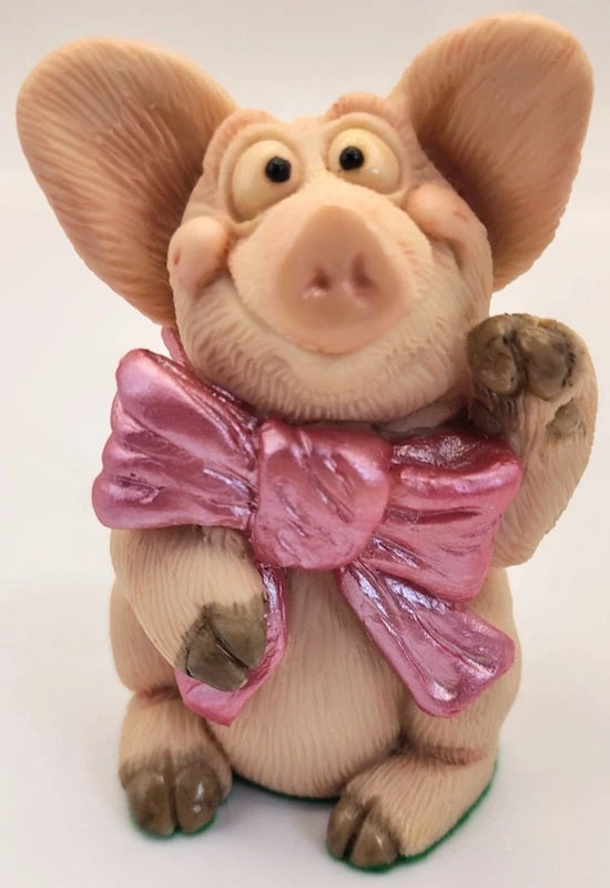 Piggin Special figurine by David Corbridge handmade in 1996. A small pig figurine with large ears, a shiny pink bow around its neck, and brown hooves, photographed against a plain light background.
