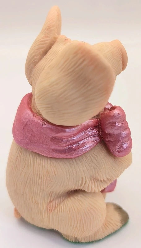 A small piggin, shaped like a seated dog or puppy, wearing a shiny pink bow scarf photographed against a plain white background.