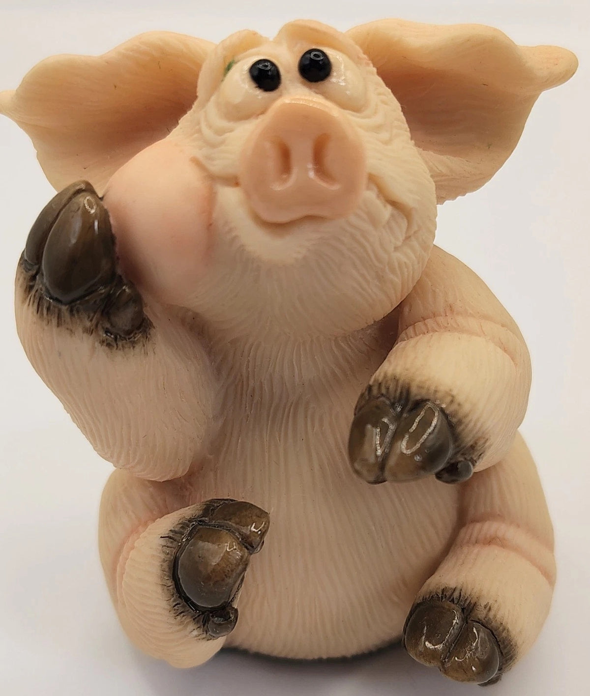 Piggin Toothache figurine by David Corbridge. A small pig figurine with a pale peach-pink body, darker pink snout and ears, black eyes, and dark brown hooves, photographed against a plain white background.