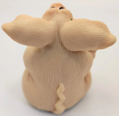 A beige ceramic figurine of a pig seen from behind, featuring detailed fur texture, small black eyes, and a small green accent near the top.