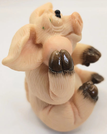 A small sculpted figurine of a pig lying on its back, with dark brown hooves and a glossy finish, photographed against a plain white background.