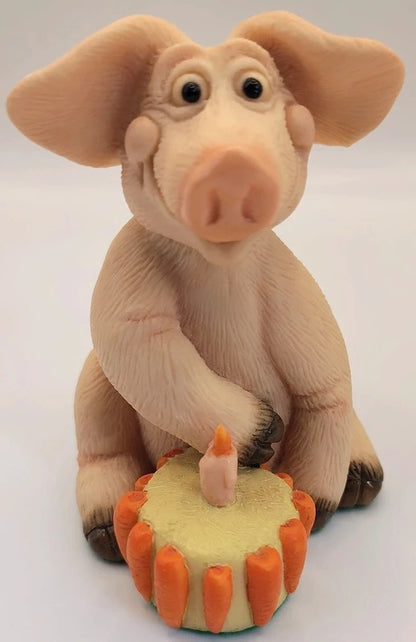Piggin Happy Birthday Figurine by David Corbridge made in 1995. A pig figurine sitting behind a small decorated cake with a single candle, photographed against a plain light background.