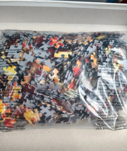 A clear plastic bag filled with many small jigsaw puzzle pieces in assorted colors, photographed against a light neutral background.