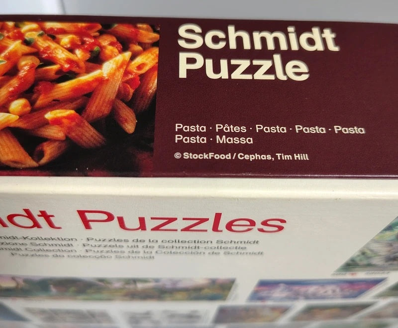 Close-up of a Schmidt Puzzles box featuring a pasta photo on a dark red panel with the title 'Schmidt Puzzle' and smaller text listing pasta varieties.