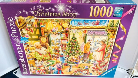 Jigsaw puzzle box featuring a Christmas scene with people and a tree, labeled 'The Christmas Shop' by Ravensburger.